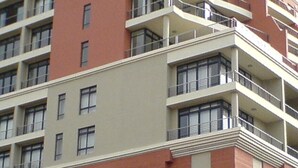 A multi-story building with balconies, large windows, and a mix of red and beige exterior walls.