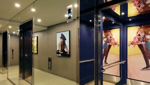 A modern elevator interior with glass doors, a digital display, and a poster on the wall. - The Kinson (Melbourne)