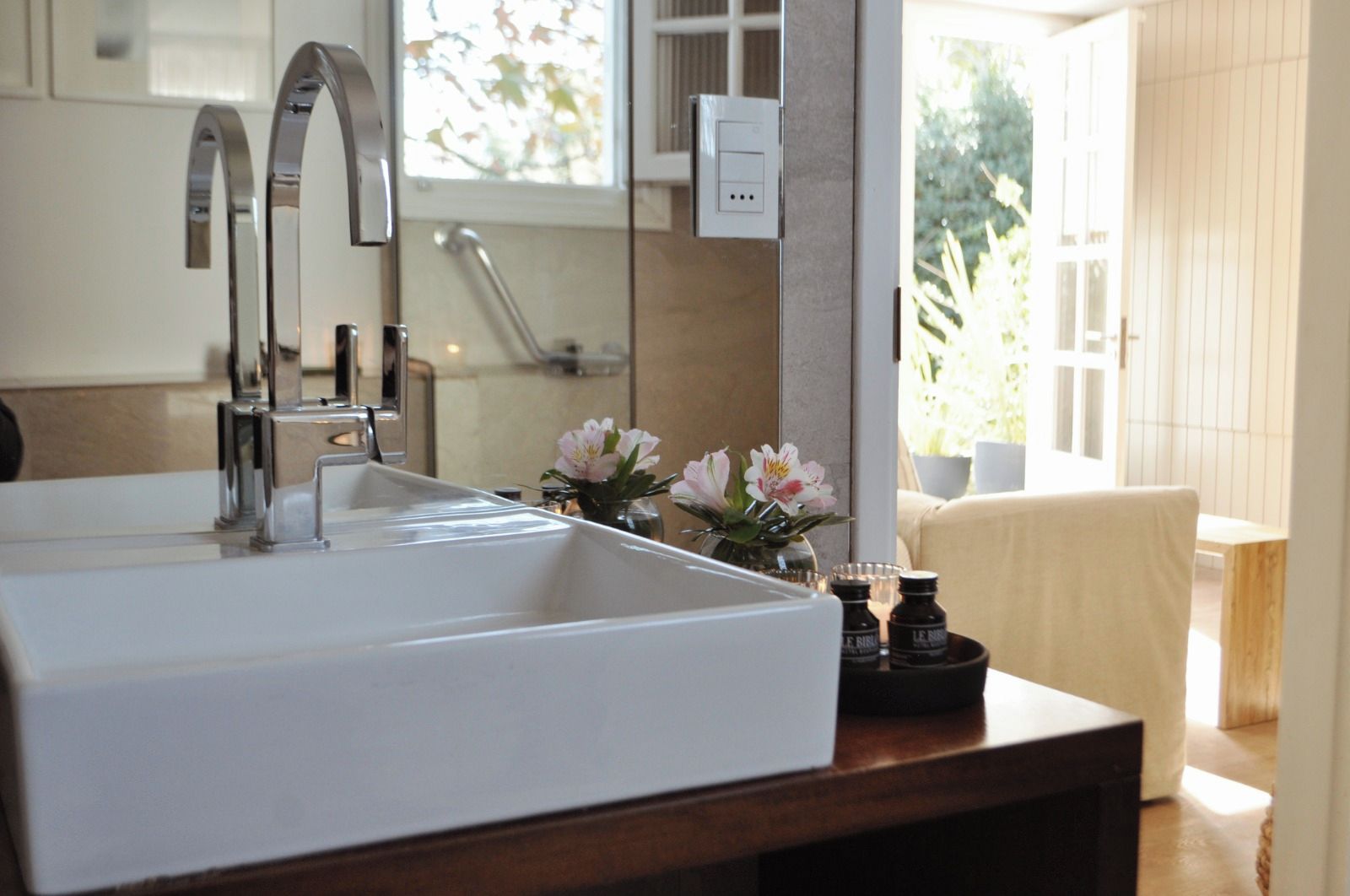 Ein Badezimmer mit einem großen weißen Waschbecken, einem modernen Wasserhahn, einem Spiegel und einem Fenster mit Blick auf Grünflächen.