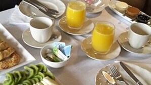 Una escena de desayuno con una bandeja de frutas, zumo de naranja y tazas de café sobre una mesa.