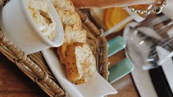A hand reaching for a bowl of dip on a tray with bread and a glass of orange juice.