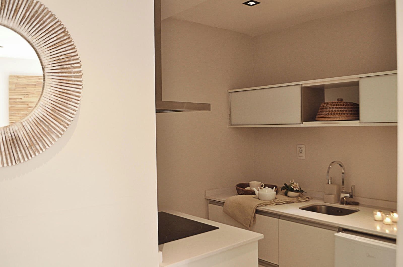 Cozinha compacta com pia, chávena e espelho decorativo.