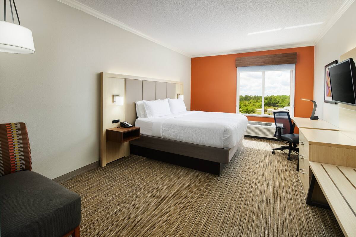 A hotel room with a bed, desk, chair, and a large window offering a view.