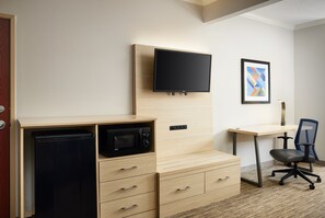 Habitación compacta con kitchenette, televisión de pantalla plana, escritorio y una silla.