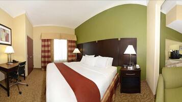 A hotel room with a large bed, two bedside tables with lamps, a desk with a chair, and a green armchair.