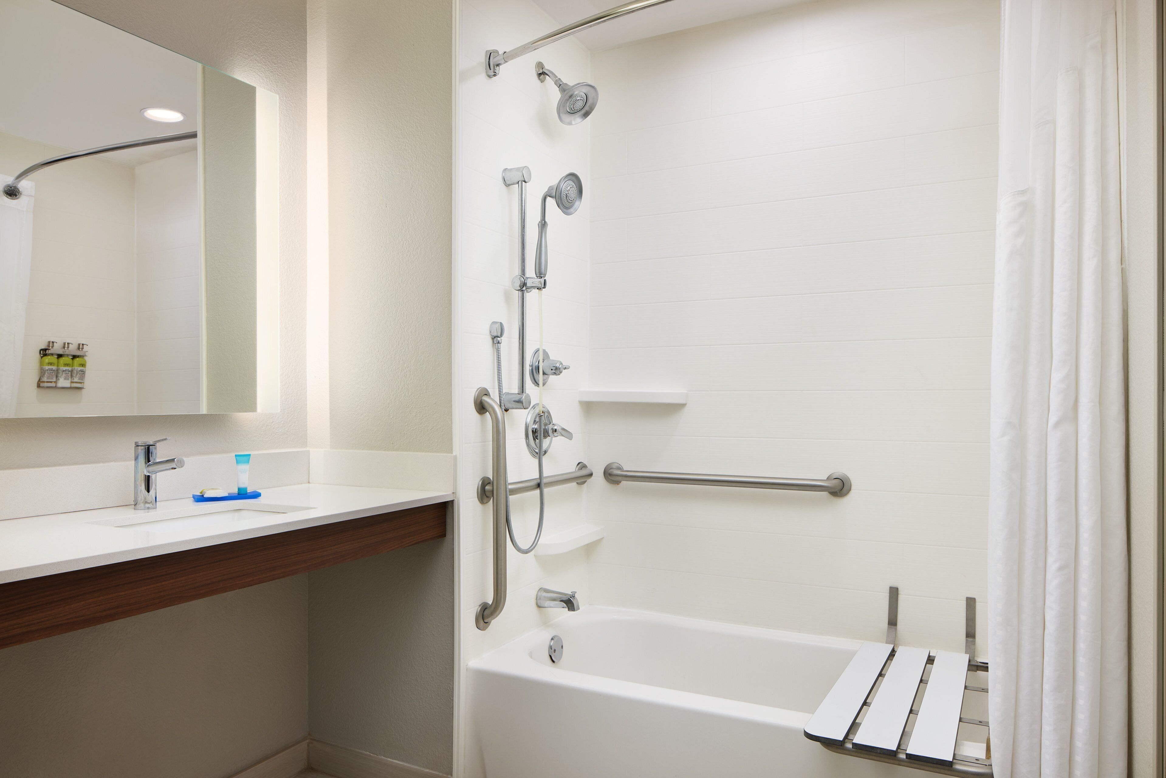 A bathroom with a white bathtub, a shower with a handheld showerhead, a grab bar, and a mirror above the sink.