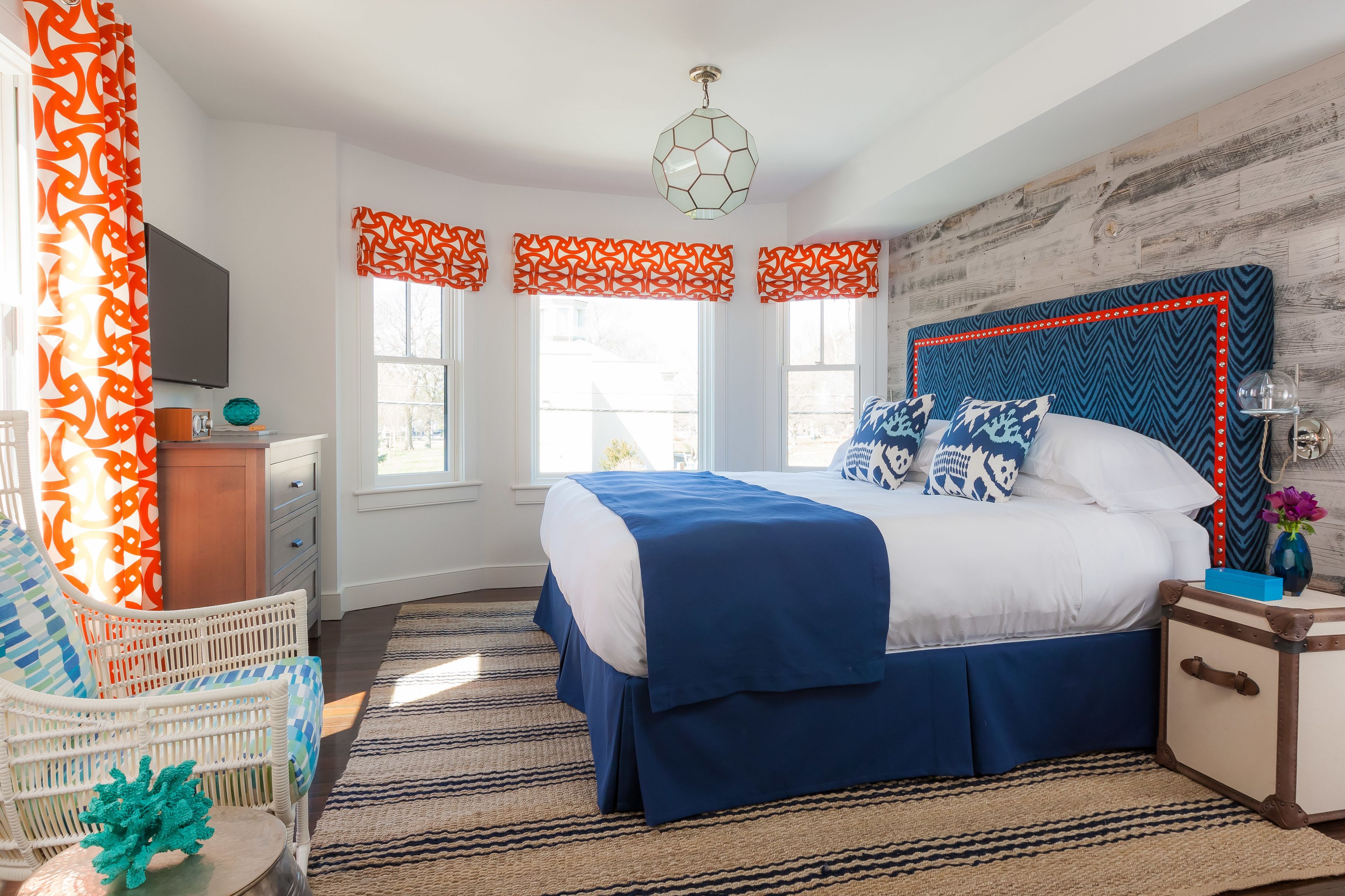 A bedroom with a bed, a chair, a nightstand, a television, and a window with curtains.