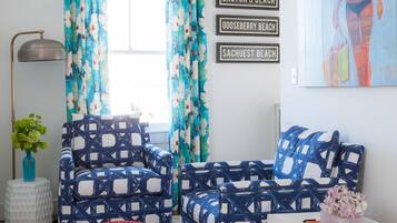 A living room with patterned armchairs, a red ottoman, and a white side table with books.