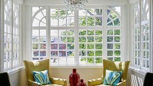 A room with two yellow armchairs, a glass table with two red vases, and a large window with a view of trees and buildings.