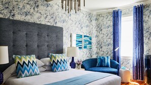 A modern hotel room with a large bed, a blue sofa, and a fireplace.