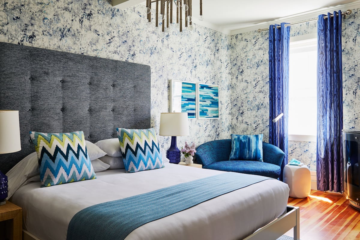 Una habitación de hotel moderna con una cama grande, un sofá azul y una chimenea.