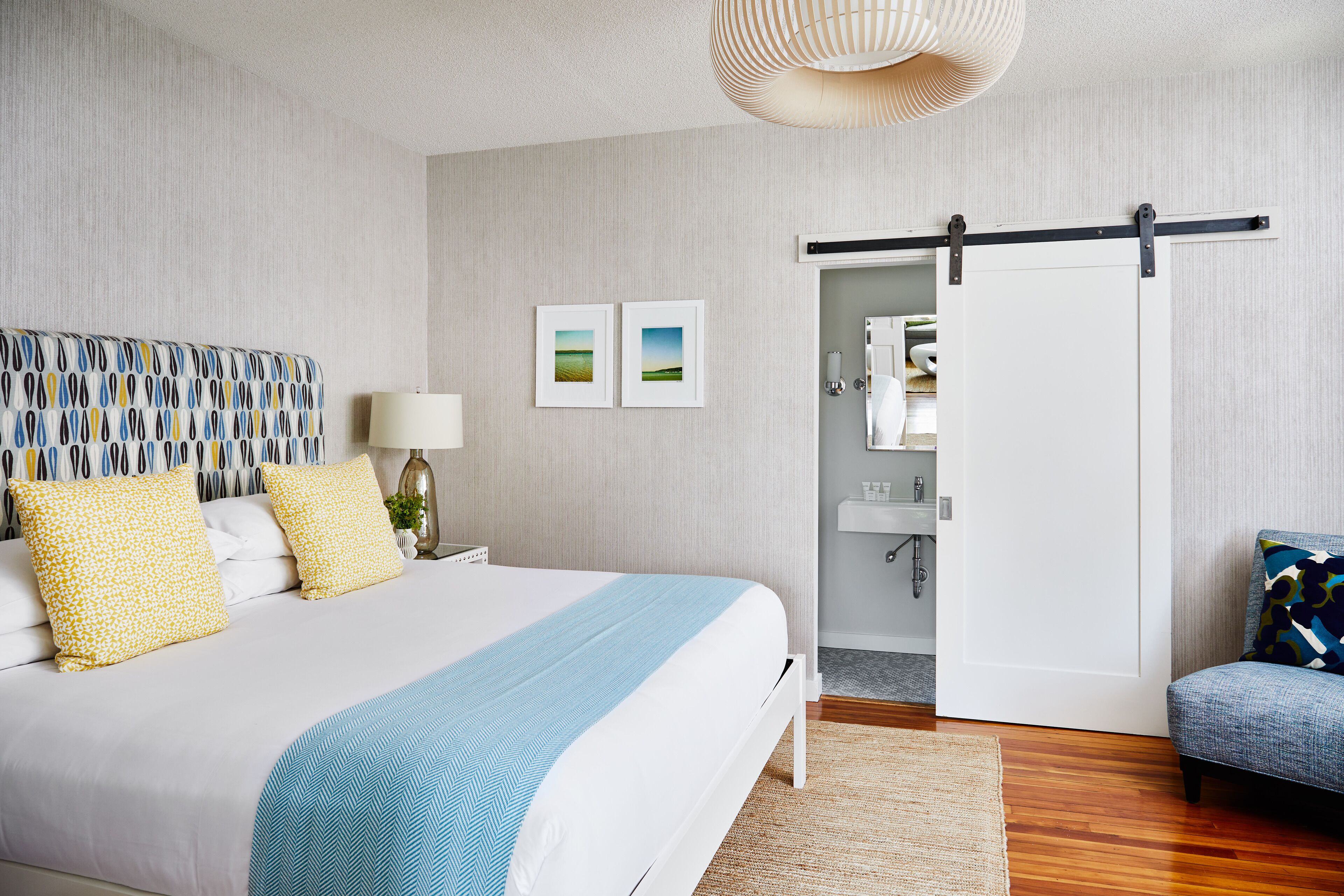 A modern bedroom with a large bed, a sofa, and a sliding door leading to a bathroom.