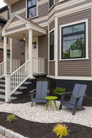 A two-story house with a covered porch, a staircase, and a small patio area with outdoor seating.