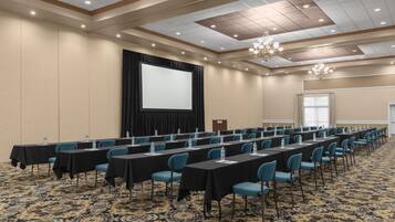 A conference room with long tables, chairs, a projector screen, and a carpeted floor.