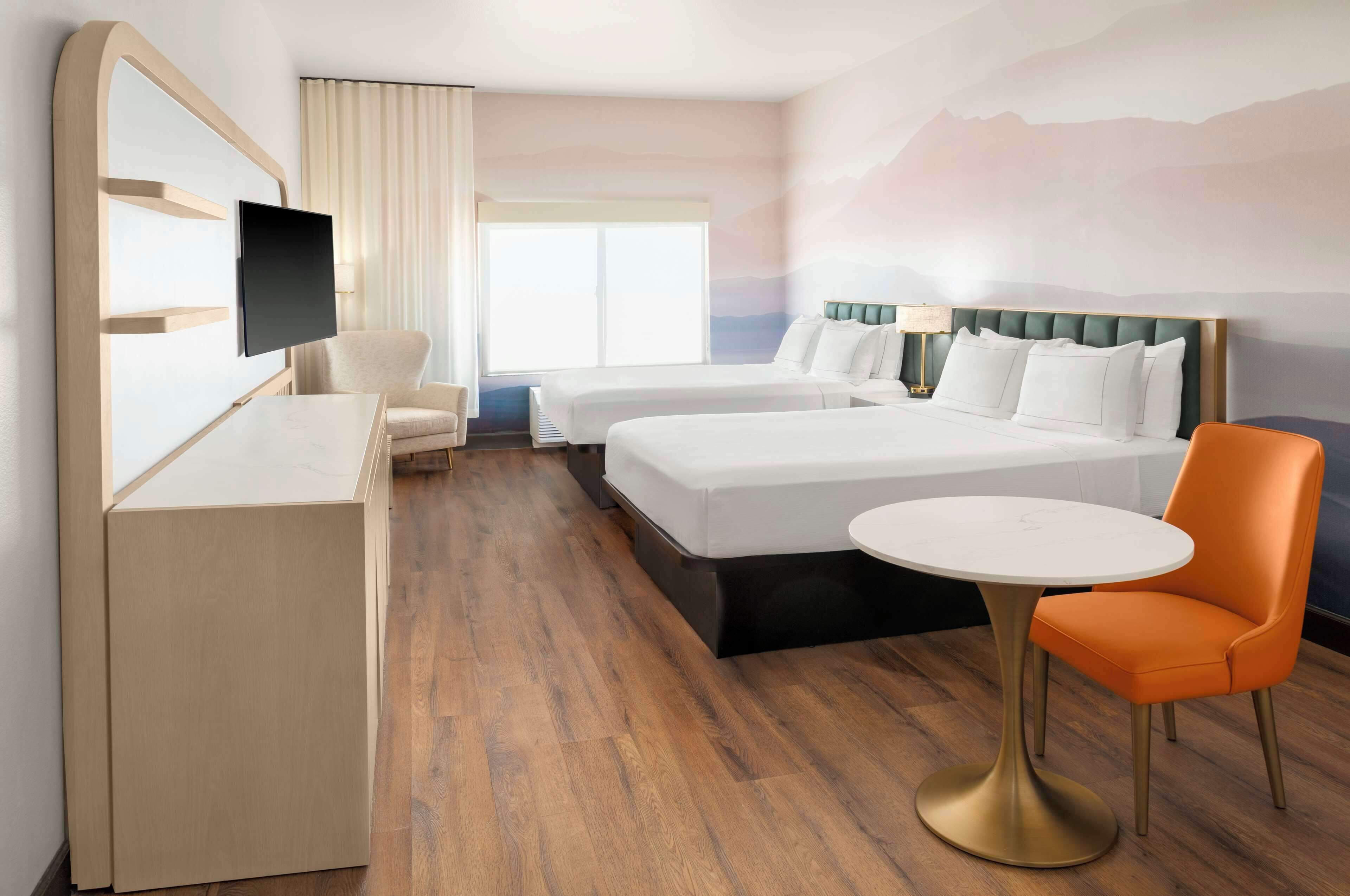 Ein Hotelzimmer mit zwei Betten, einem Schreibtisch, einem Stuhl und einem runden Tisch.