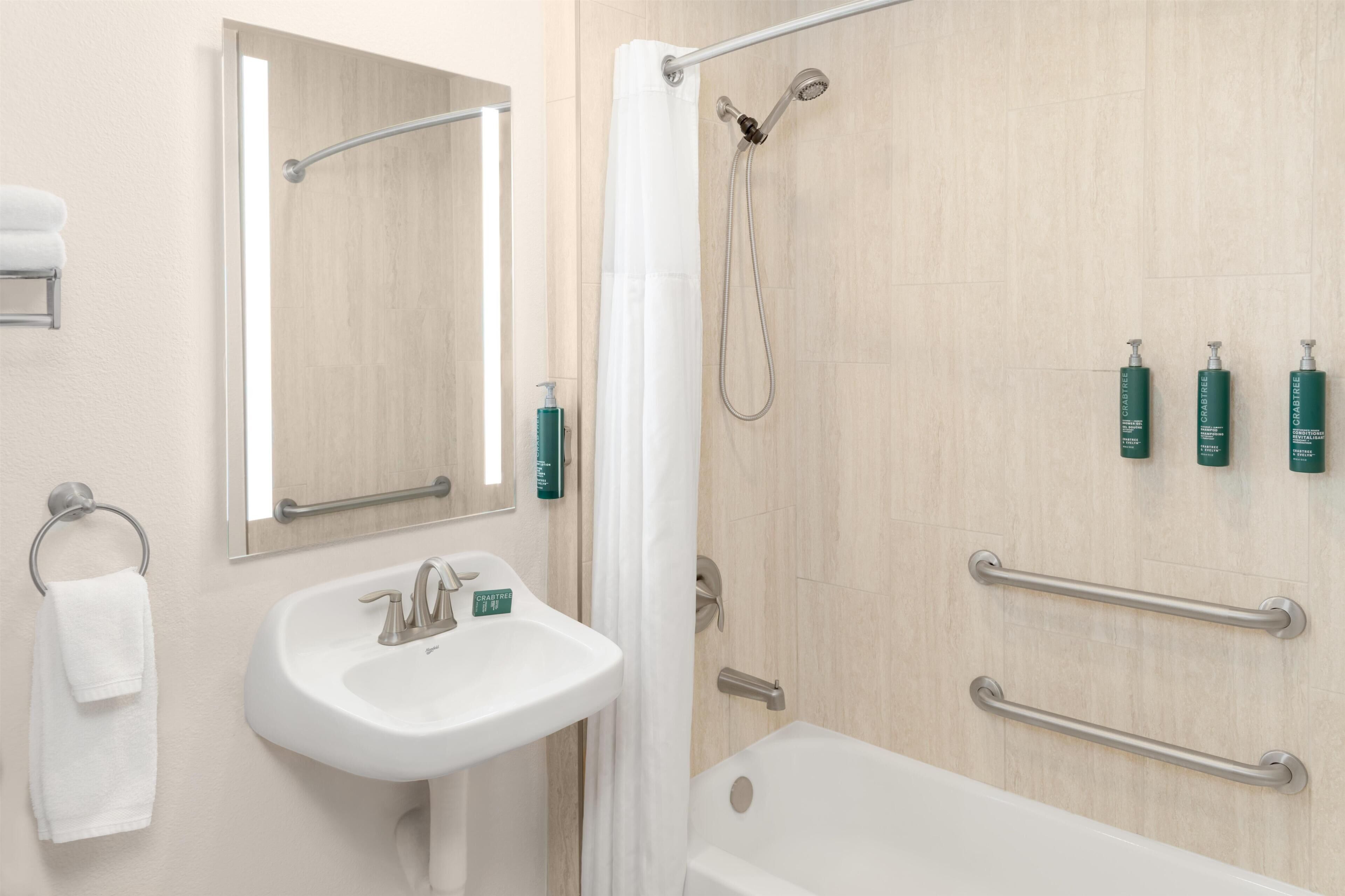 A bathroom with a sink, mirror, shower, and grab bars.