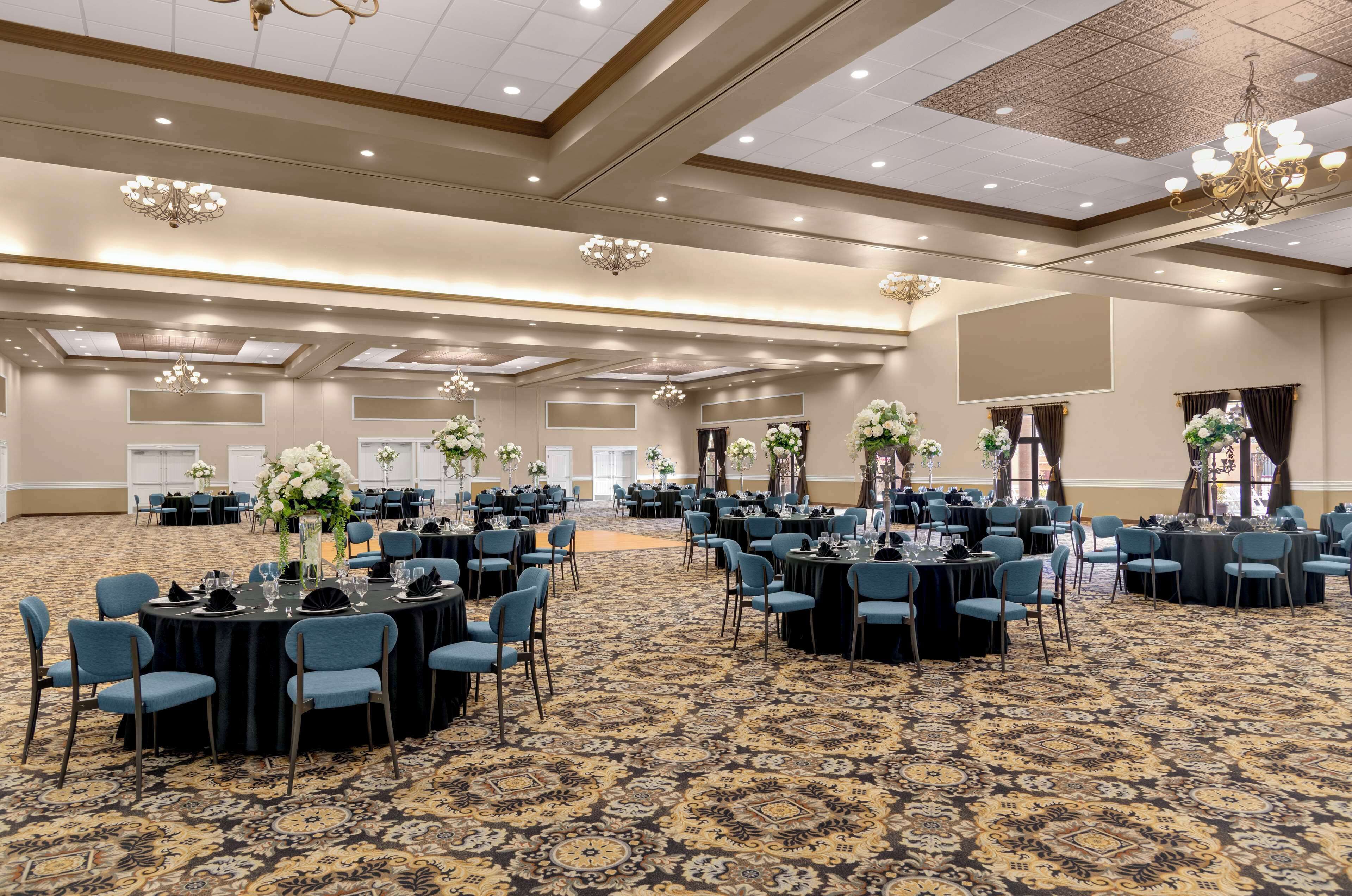 A large banquet hall with round tables, blue chairs, and floral centerpieces.