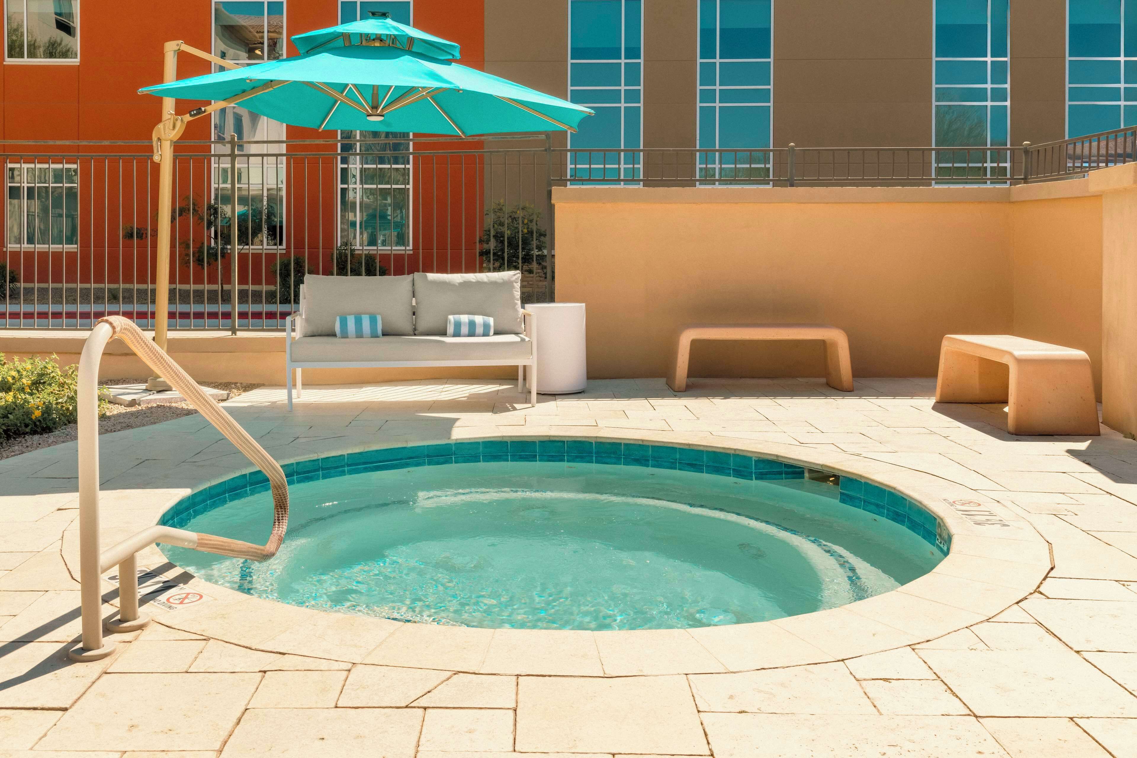 A swimming pool with a lounge area, including a sofa and a small table, and a large umbrella providing shade.