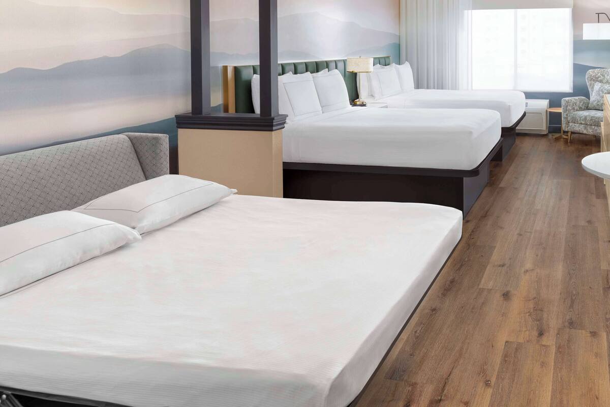 A hotel room with two beds, a sofa, a chair, and a desk.