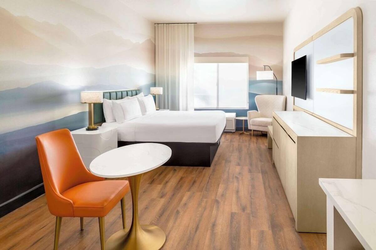 A hotel room with a bed, a desk, a chair, a TV, and a view of the mountains.