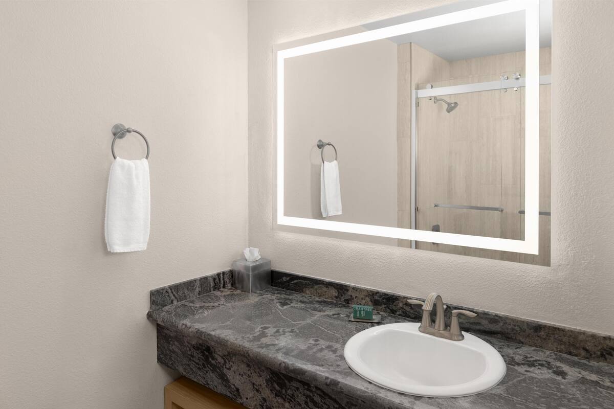 A bathroom with a marble countertop, a white sink, a mirror with a lighted frame, and a towel rack.