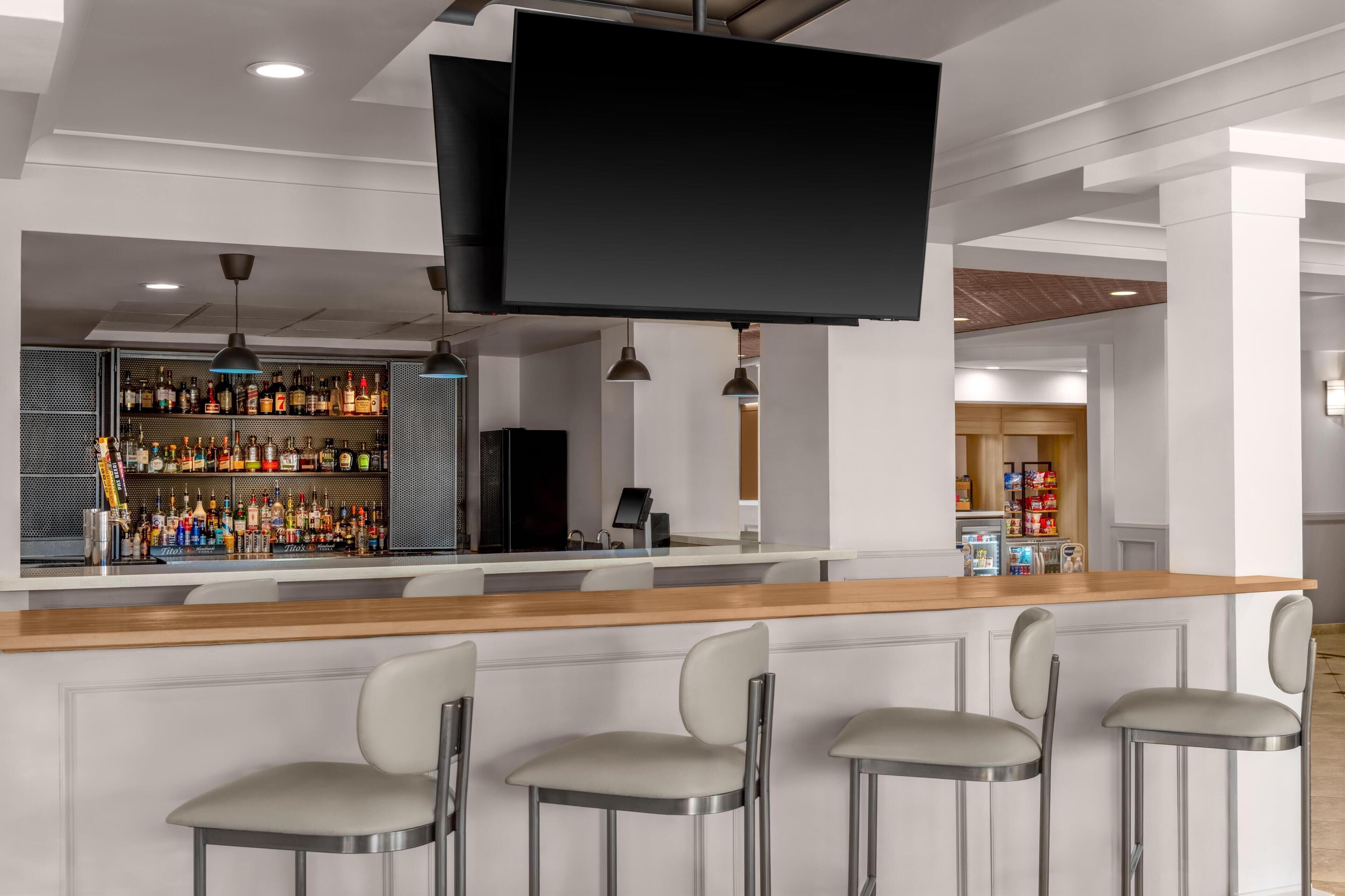 A bar area with a long counter, multiple bar stools, and a television screen.