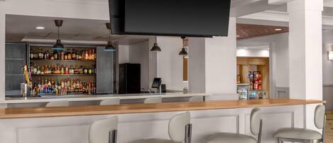 A bar area with a long counter, multiple bar stools, and a television screen.