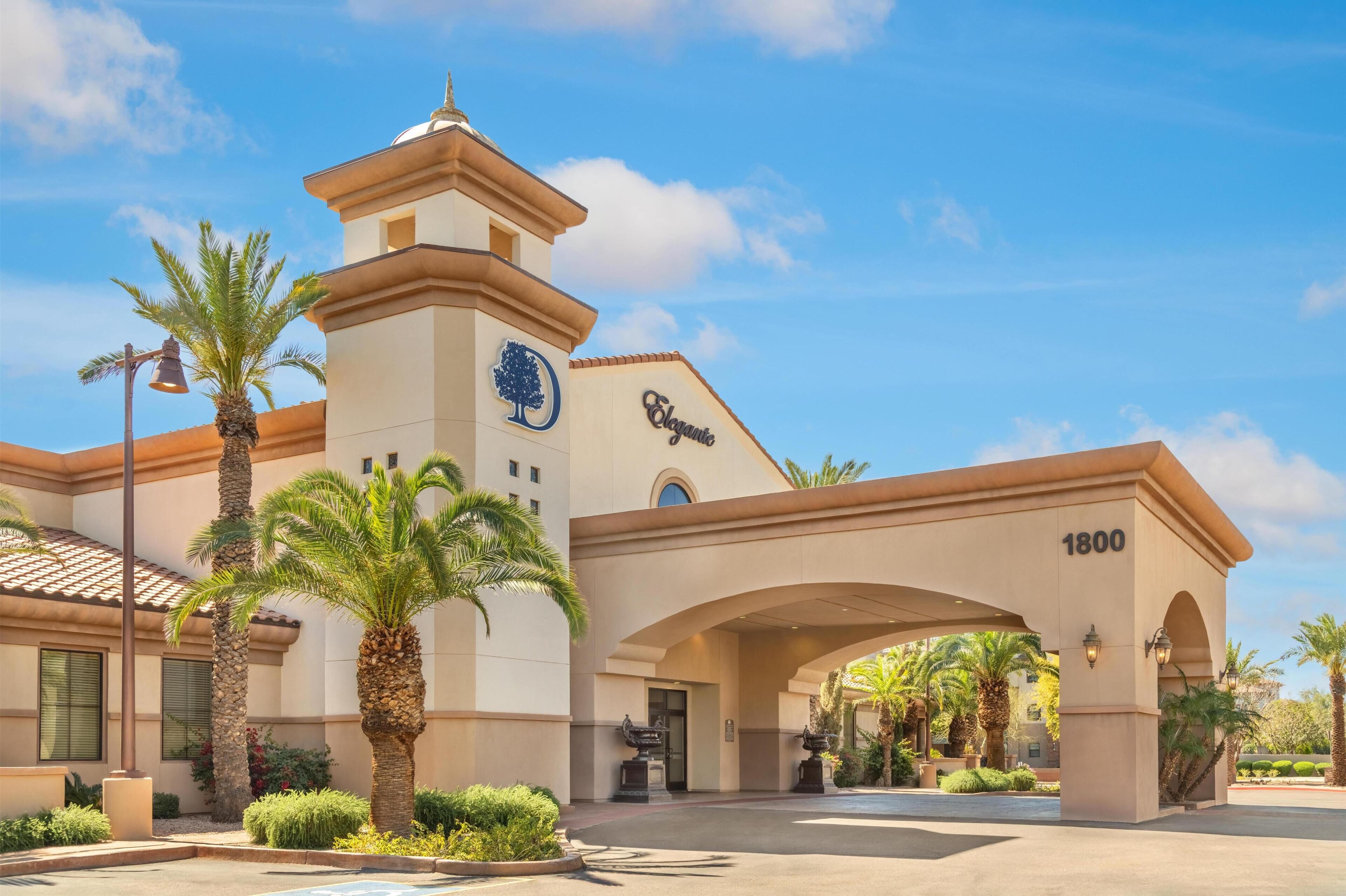 A hotel entrance with a prominent archway, a clock tower, and palm trees.