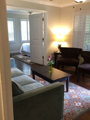 Una sala de estar con sofá, mesa de centro y lámpara. Hay una puerta que da a otra habitación.