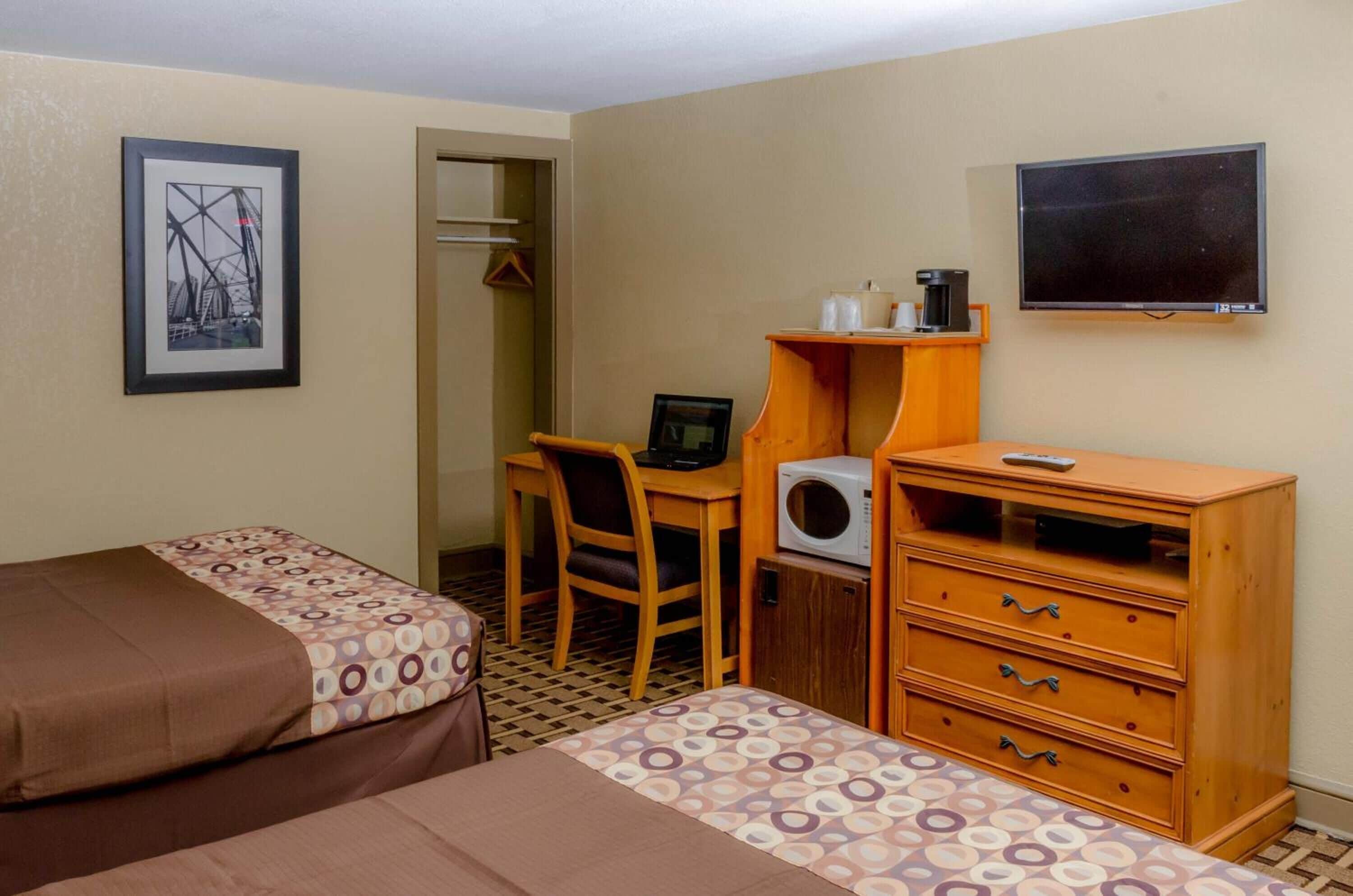Une chambre d’hôtel avec deux lits, un bureau avec une chaise, un four à micro-ondes, une commode en bois et un téléviseur fixé au mur.