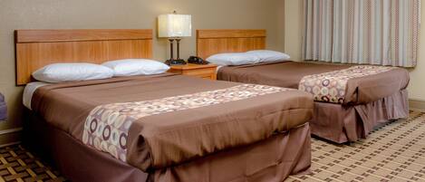 Habitación de hotel con dos camas, una mesita de noche, una lámpara y una alfombra estampada.
