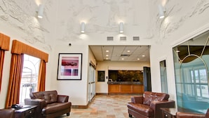 A lobby with leather sofas, a framed picture, a reception desk, and a stone wall. - Canalta Hotel Jurassic – Drumheller (Drumheller)