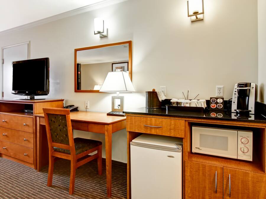 Une chambre d’hôtel équipée d’un bureau en bois, d’une télévision, d’une lampe, d’un four à micro-ondes, d’une machine à café et d’un mini-réfrigérateur.