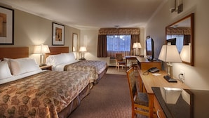 A hotel room with two beds, a desk with a computer, a chair, and a desk lamp. - Canalta Hotel Jurassic – Drumheller (Drumheller)
