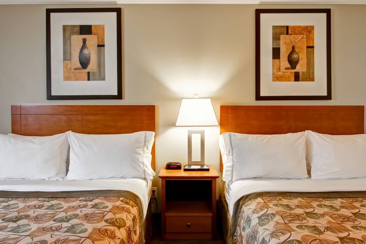 A hotel room with two beds, a nightstand with a lamp, and framed artwork on the walls.