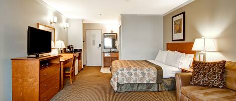 A hotel room with a bed, a desk with a television, a sofa, and a mirror.