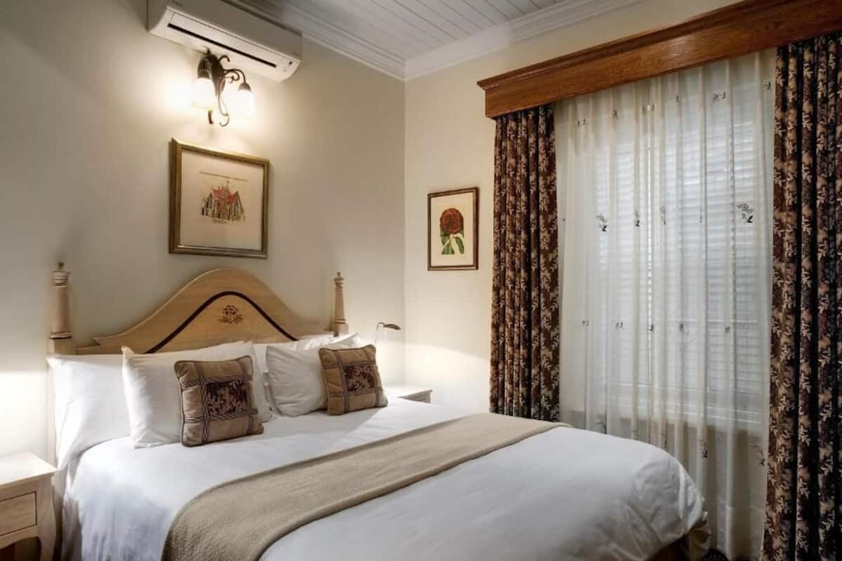 A neatly made bed with a wooden headboard, two wall-mounted lamps, and framed pictures on the wall.