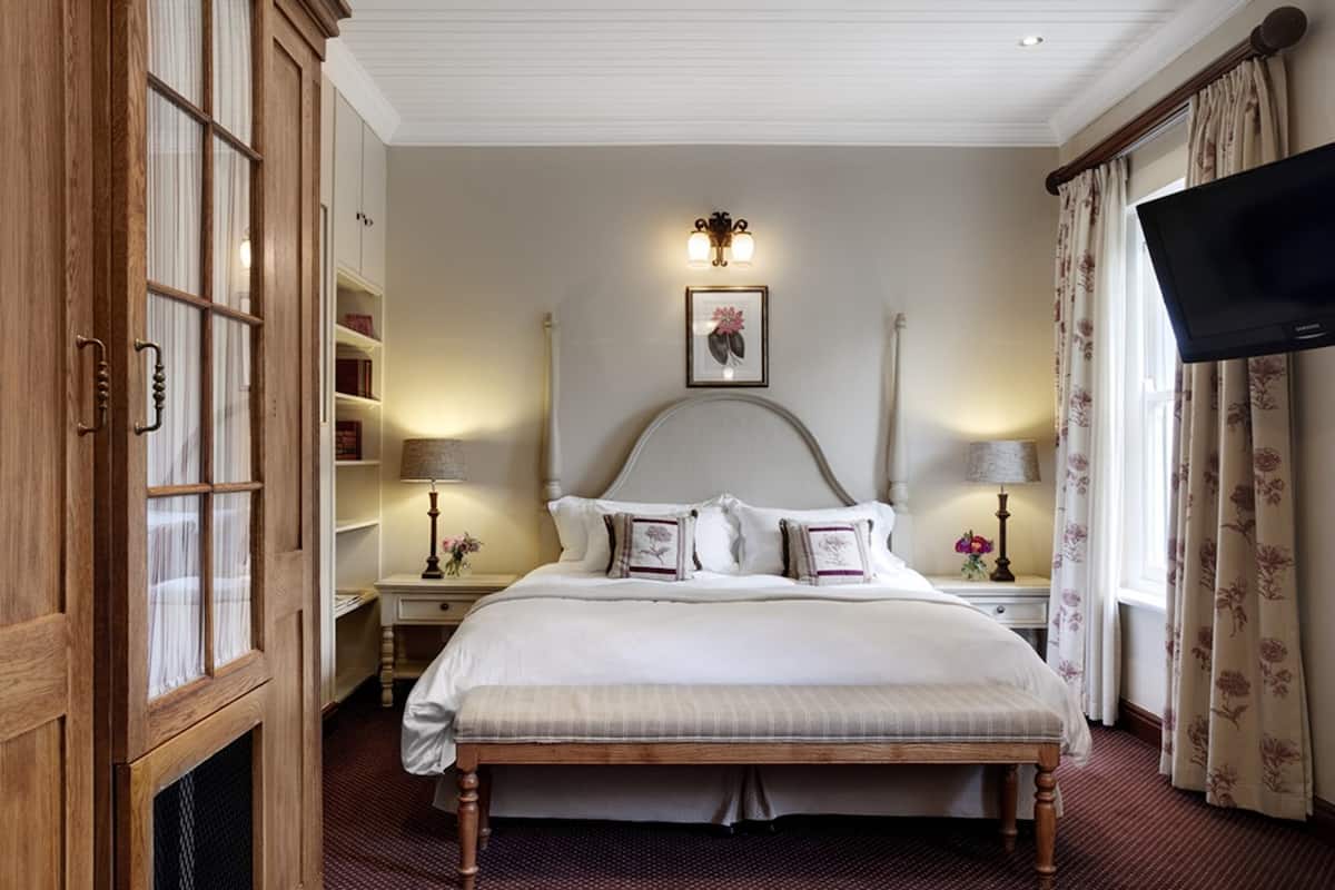 A bedroom with a large bed, wooden wardrobe, bedside tables with lamps, a flat-screen TV, and a framed picture on the wall.
