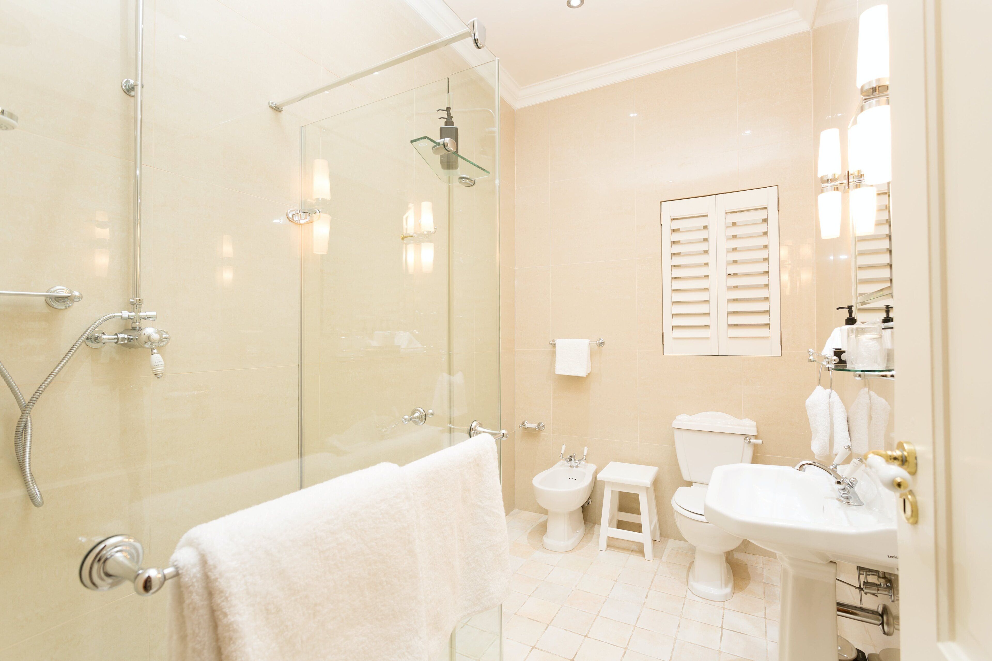 A modern bathroom with a glass-enclosed shower, a toilet, a sink, and a small stool.