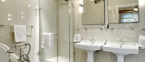 A modern bathroom with a glass-enclosed shower, two pedestal sinks, and a large mirror above the sinks.