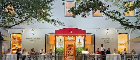 El exterior del hotel Coopmanhuijs, con un toldo rojo, un área de comedor al aire libre y huéspedes sentados en mesas.