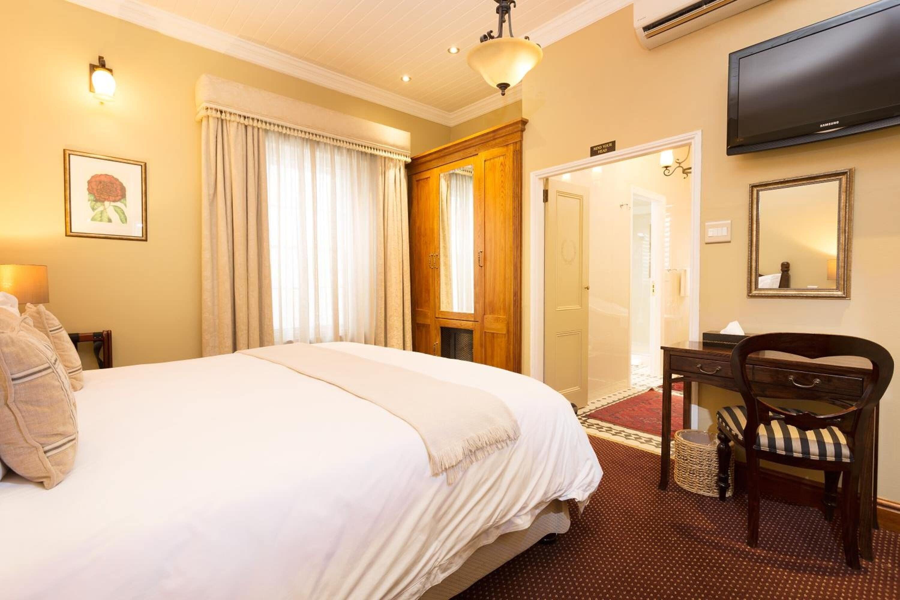 A hotel room with a large bed, a desk with a chair, a television, and a mirror.