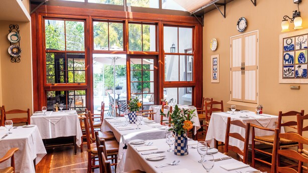 A restaurant with multiple tables set for dining, large windows, and a view of the outdoors. - Coopmanhuijs Boutique Hotel (Stellenbosch)