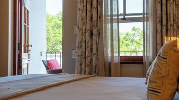 A bedroom with a bed, a window with curtains, a chair, and a view of greenery outside.