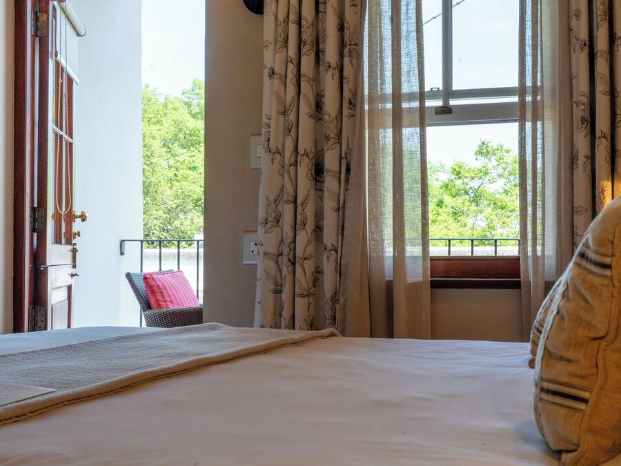 A bedroom with a bed, a window with curtains, a chair, and a view of greenery outside.