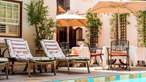 A poolside area with lounge chairs and umbrellas, a tiled pool edge, and a building with a window and shutters. - Coopmanhuijs Boutique Hotel (Stellenbosch)