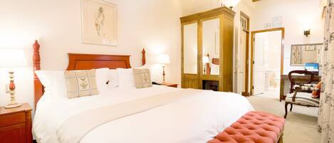 A neatly arranged bedroom with a large bed, a wooden wardrobe, a mirror, and a chair.