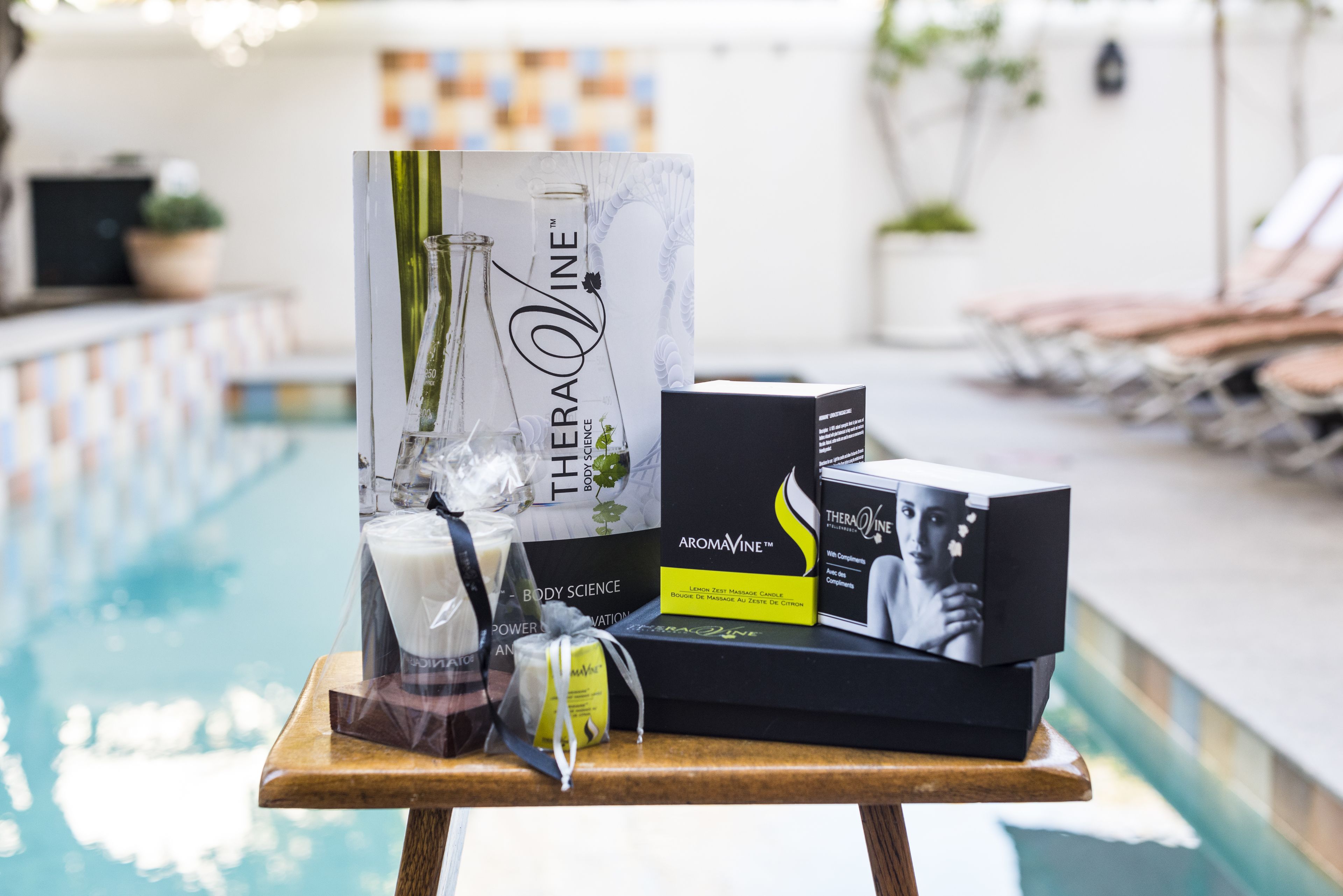 Zona de piscina con una mesa que exhibe varios productos, incluyendo una botella de loción corporal Science Body y una caja de aromavine Science Body.