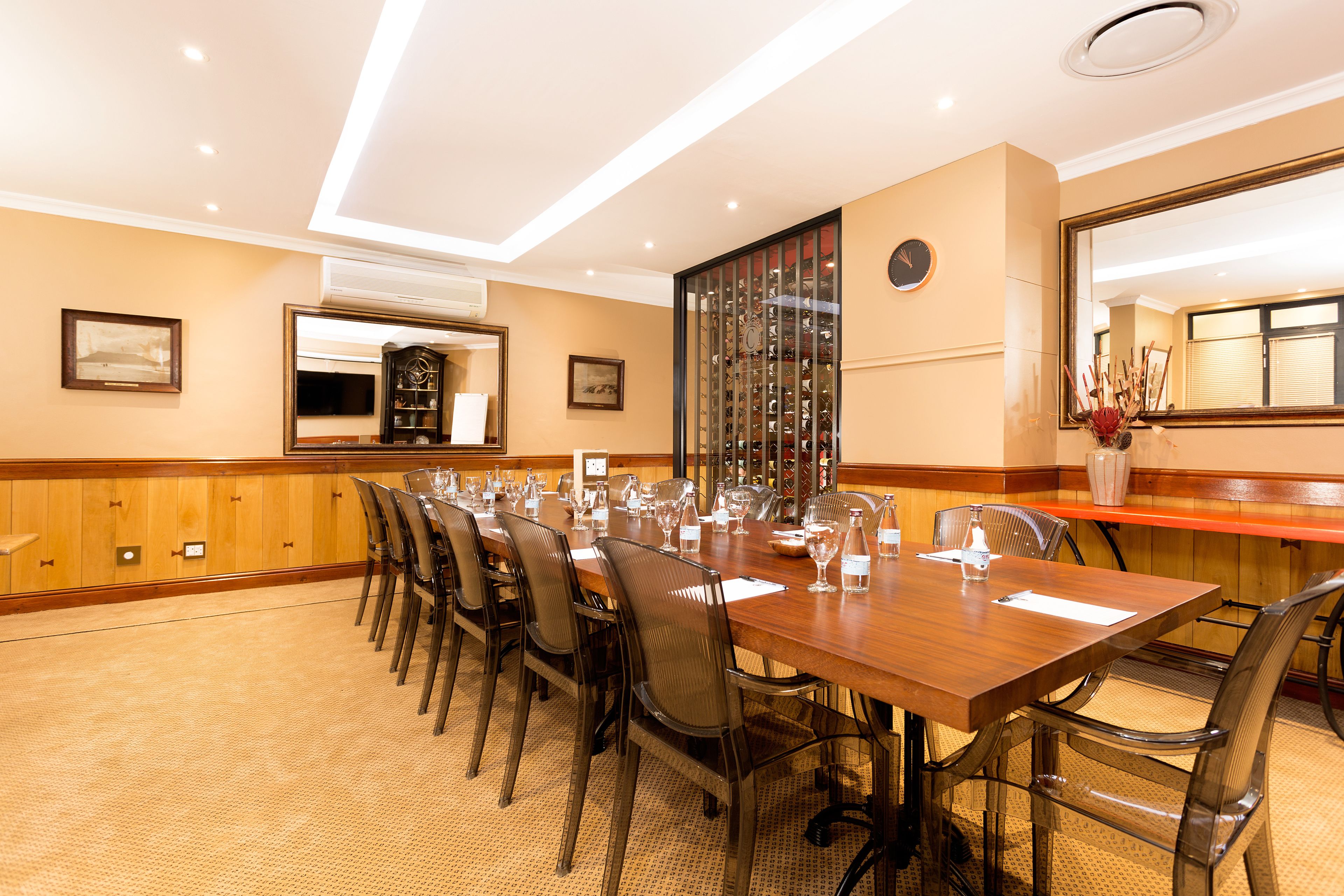 Un salón de conferencias con una larga mesa de madera, sillas y un espejo grande.