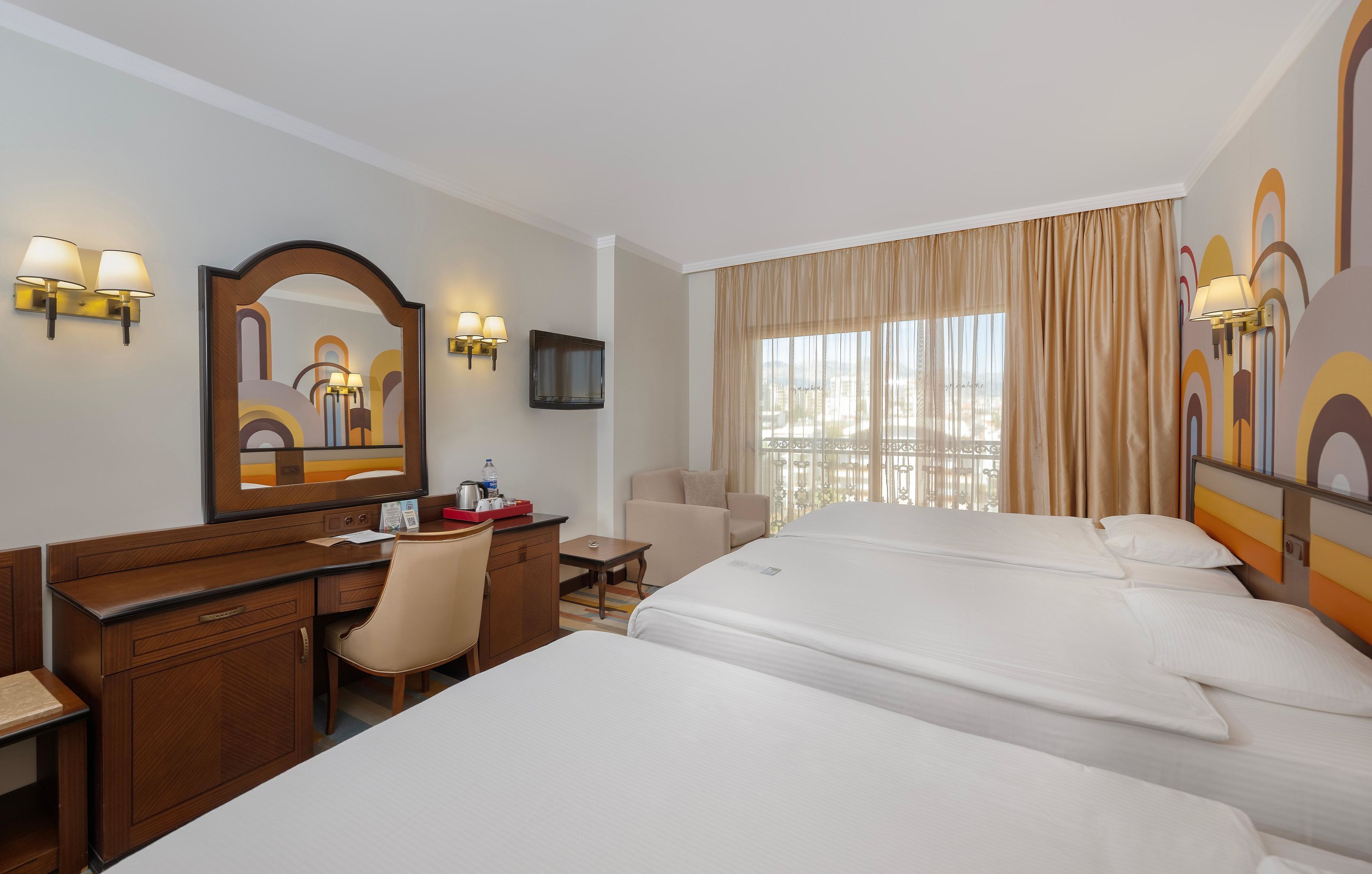 A hotel room with two beds, a desk, a chair, a TV, and a large window with curtains.